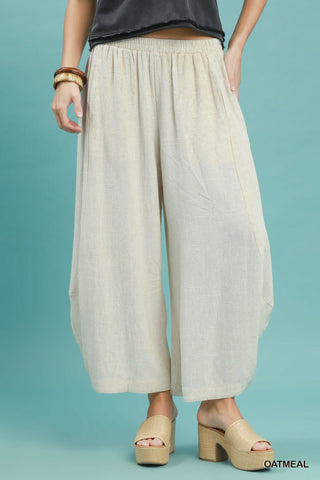 Women wearing linen oatmeal coloured pants on a blue background.