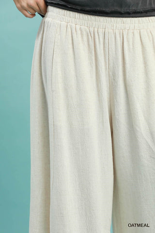 Women wearing linen oatmeal coloured pants on a blue background.