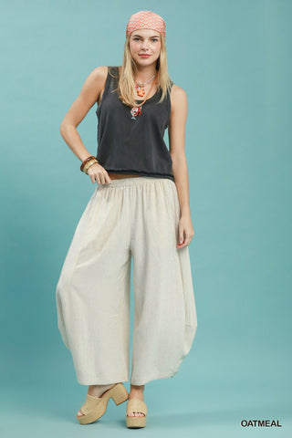 Women wearing linen oatmeal coloured pants on a blue background.