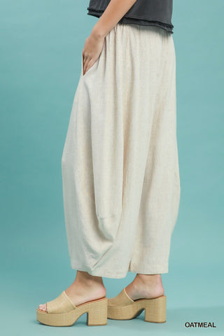 Women wearing linen oatmeal coloured pants on a blue background.