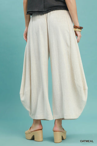 Women wearing linen oatmeal coloured pants on a blue background.
