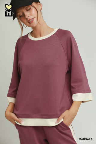 Woman wearing a maroon sweatshirt with white trim on a plain background