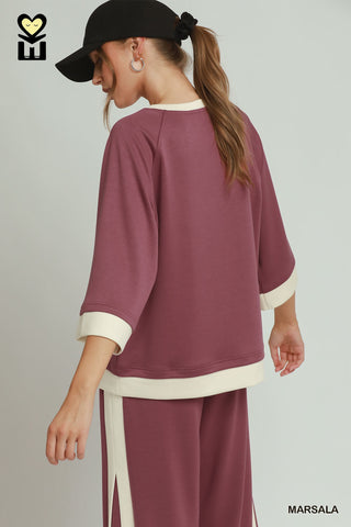 Woman wearing a maroon outfit with white accents on a plain background