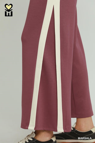 Maroon pants with a white stripe worn by a person on a plain background