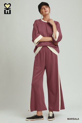 Woman wearing a maroon outfit with white accents on a plain background