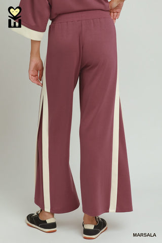 Maroon pants with white stripes worn by a person on a plain background