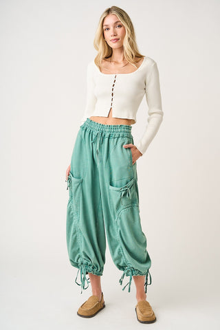 Woman wearing a white top and teal high-waisted pants on a white background