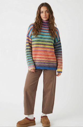 Woman wearing a colorful striped sweater and brown pants on a white background