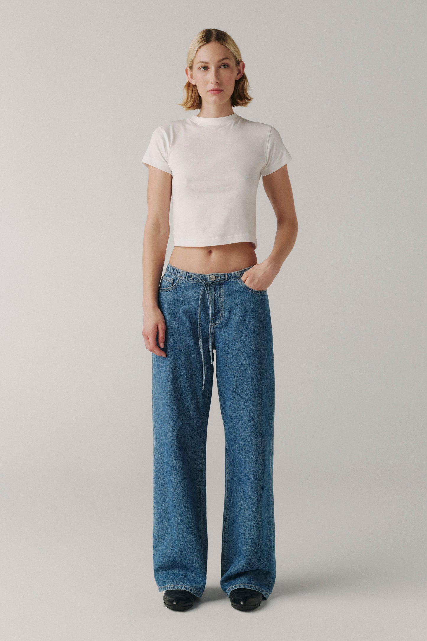 Person wearing a white crop top and blue jeans on a plain background