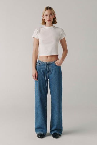 Person wearing a white crop top and blue jeans on a plain background