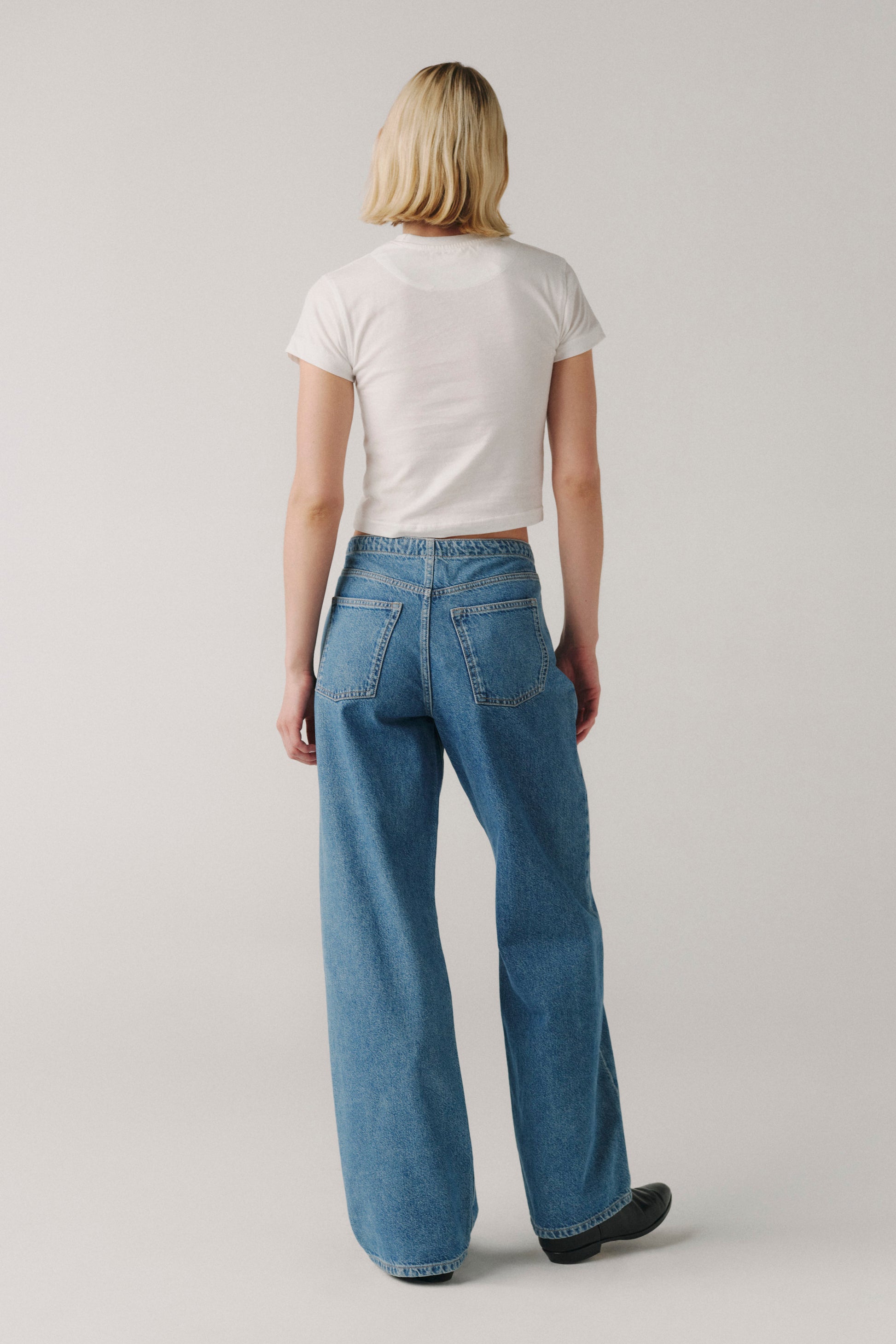 Person wearing a white t-shirt and blue jeans on a plain background