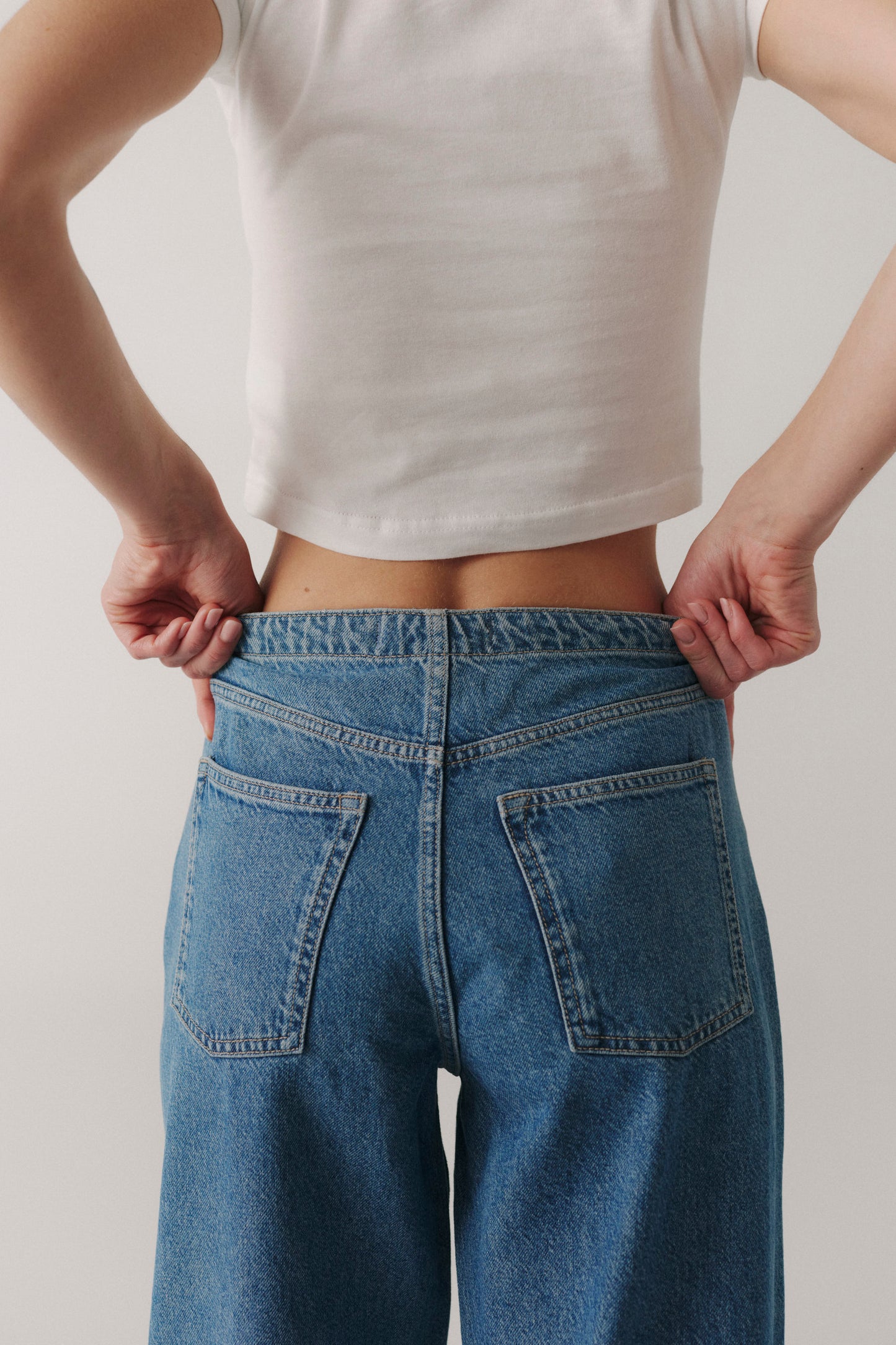 Person wearing a white crop top and blue jeans against a plain background