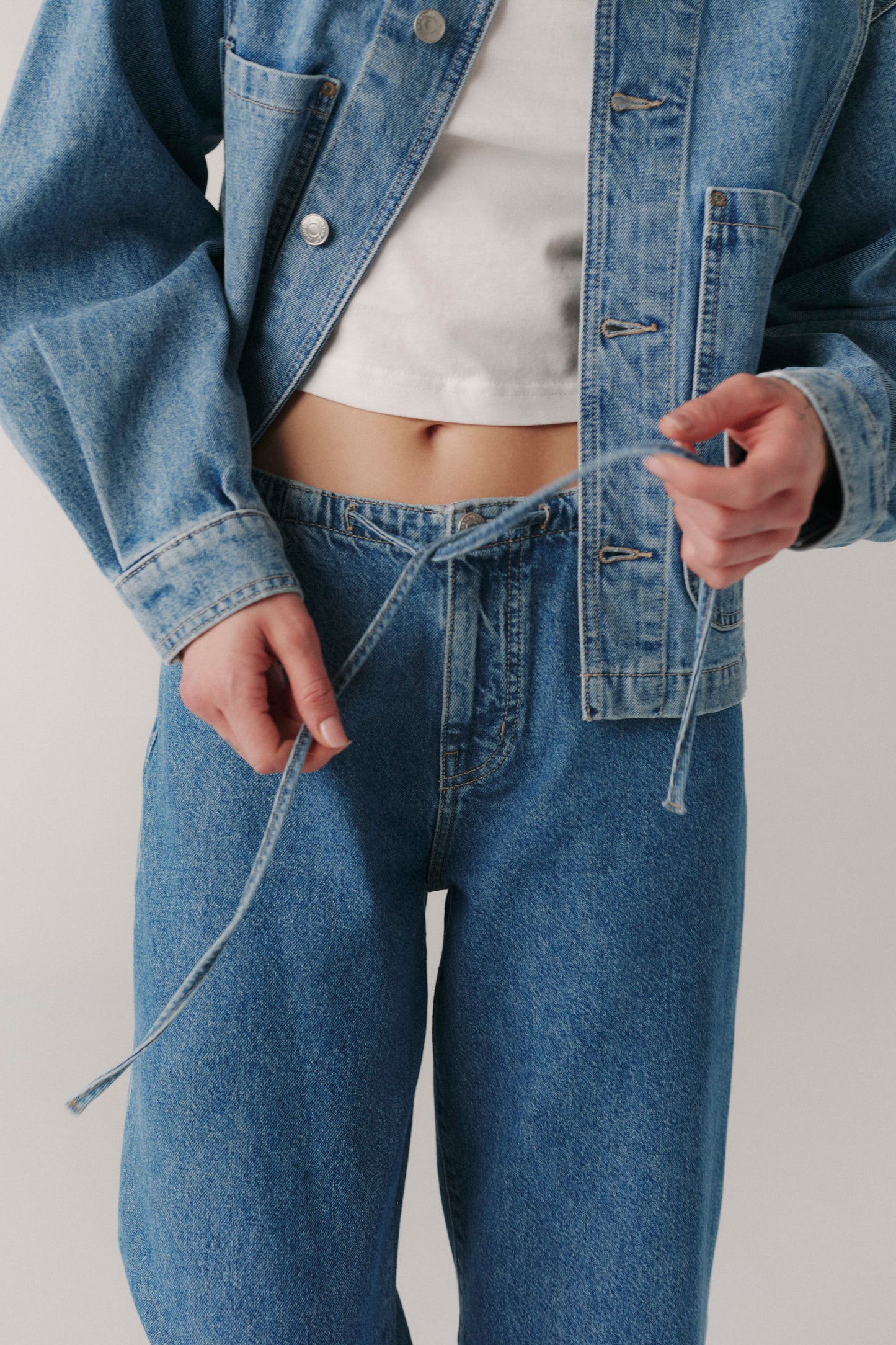 Person wearing a denim jacket and jeans on a plain background