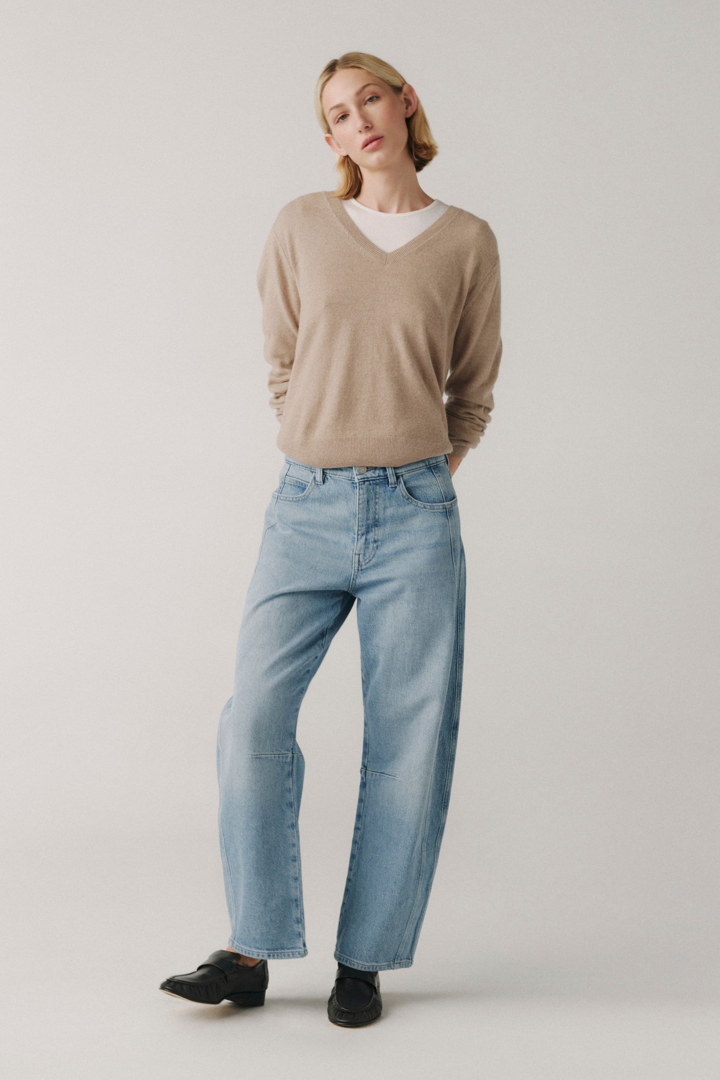 Woman wearing a beige sweater and light blue jeans on a plain background