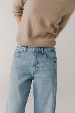 Person wearing a beige sweater and light blue jeans on a plain background