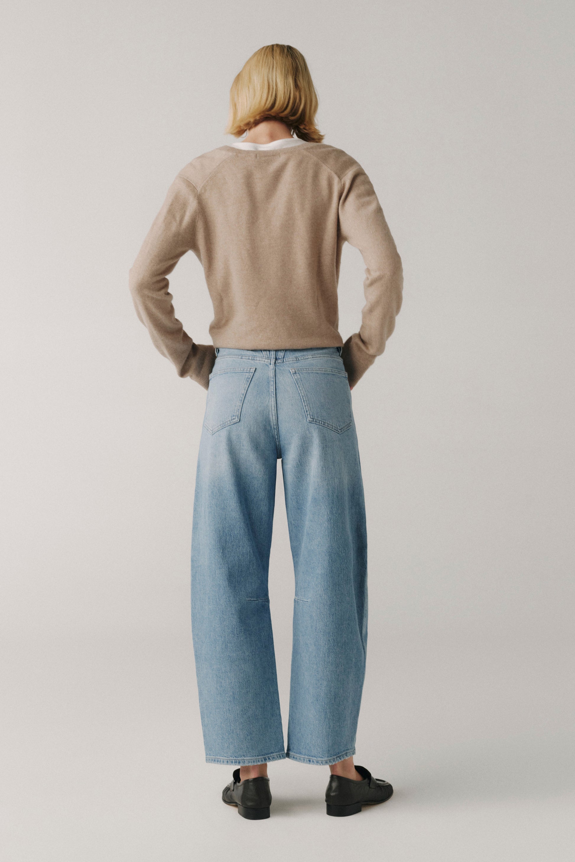 Person wearing a beige sweater and light blue jeans on a plain background
