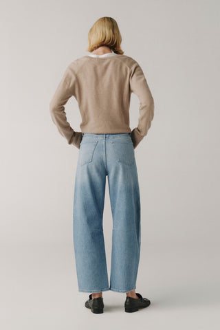 Person wearing a beige sweater and light blue jeans on a plain background