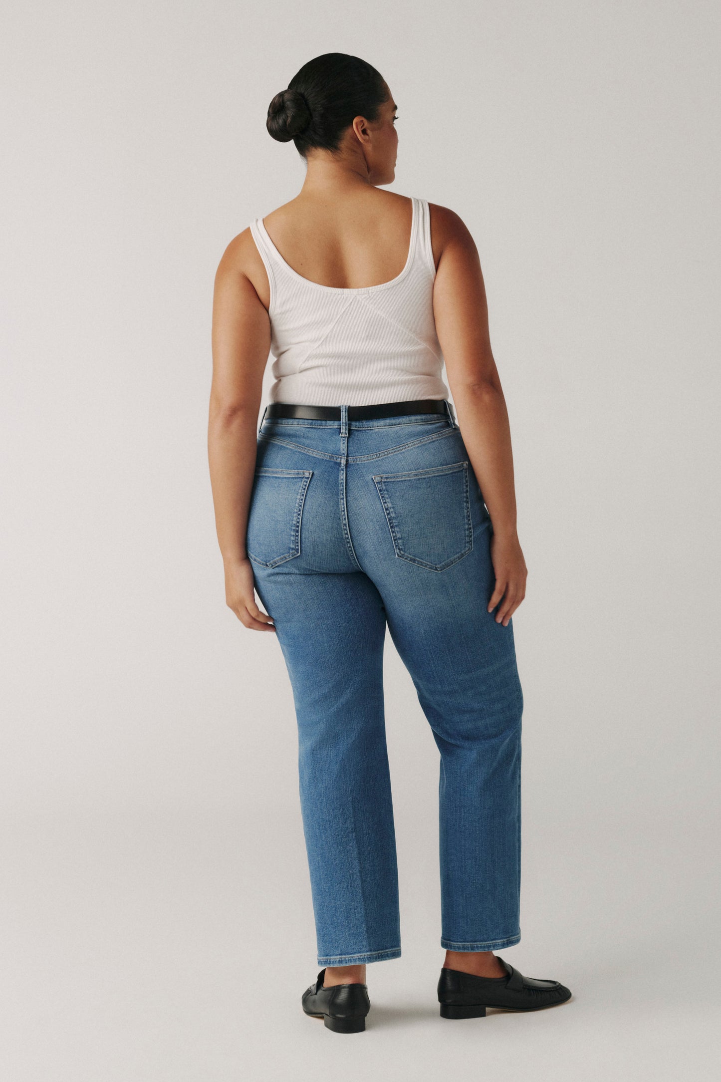 Person wearing blue jeans and a white tank top on a plain background