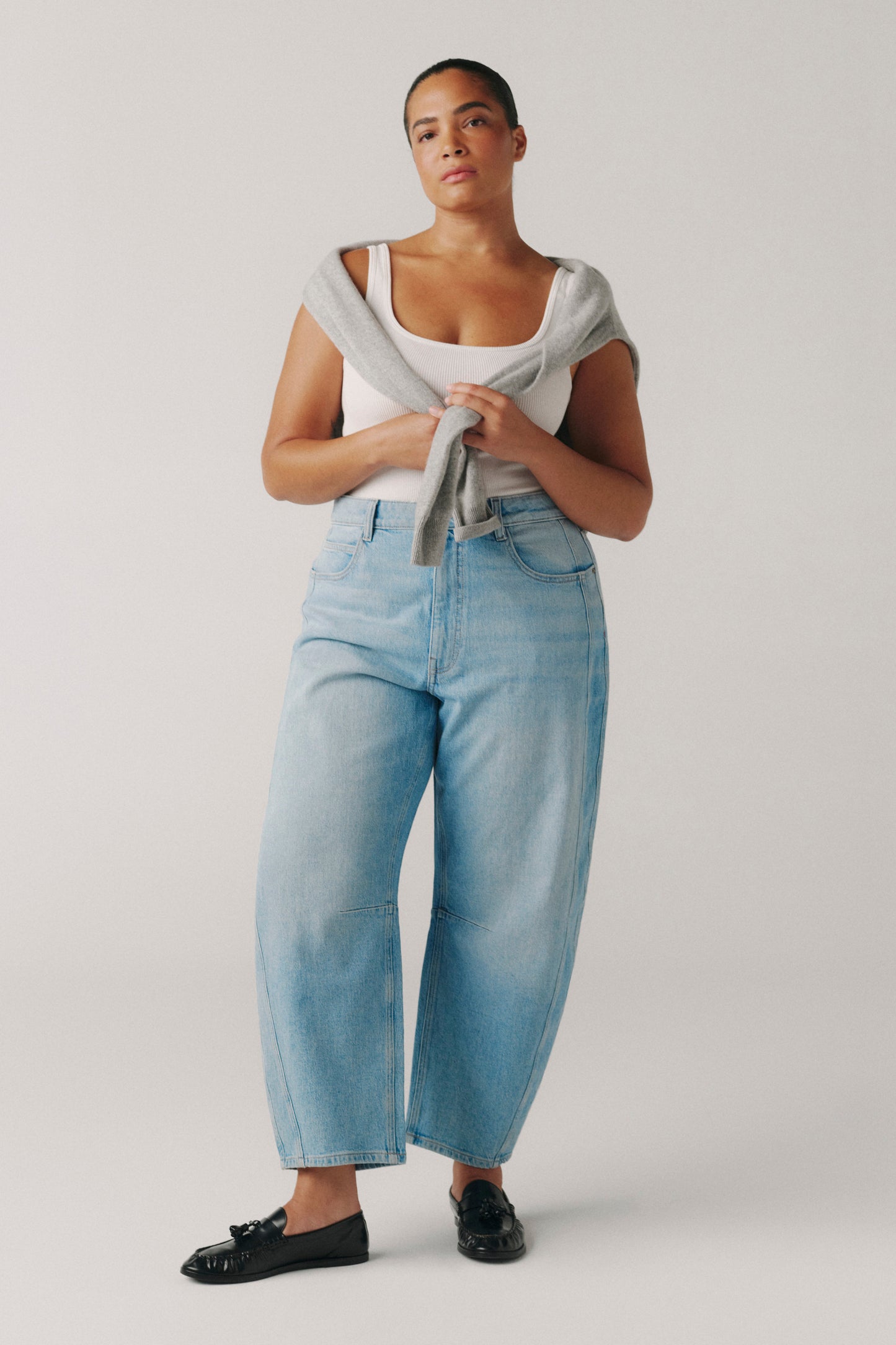 Person wearing a white tank top and light blue jeans on a plain background