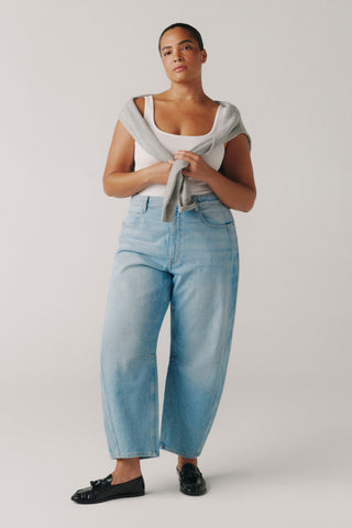 Person wearing a white tank top and light blue jeans on a plain background