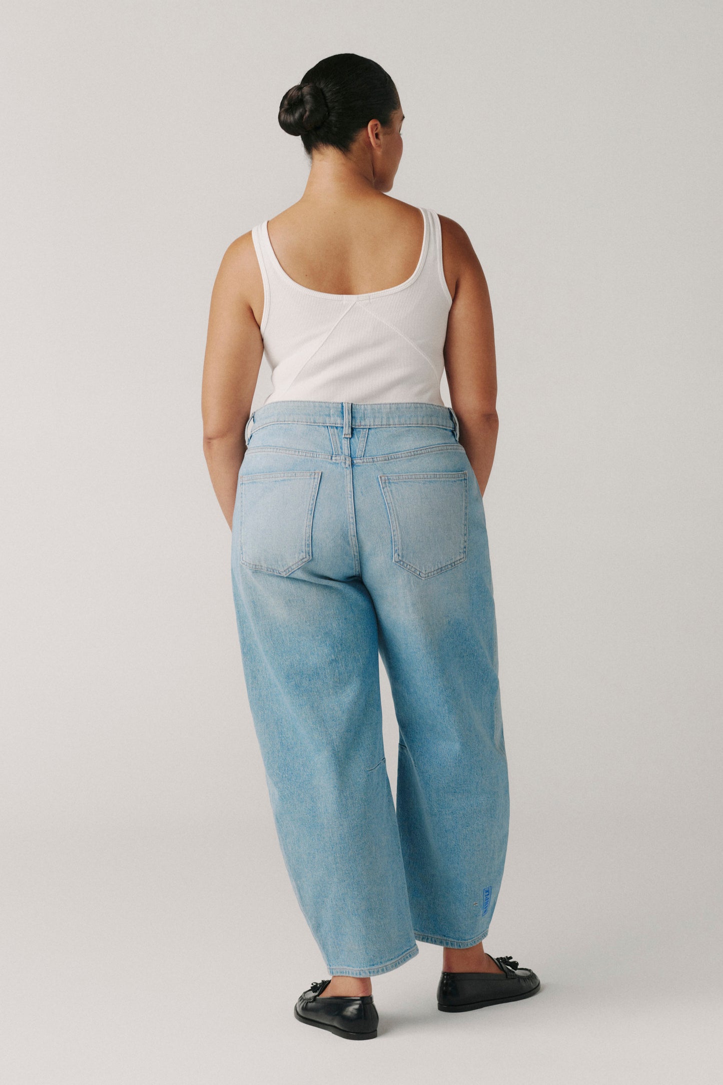 Person wearing a white tank top and light blue jeans on a plain background