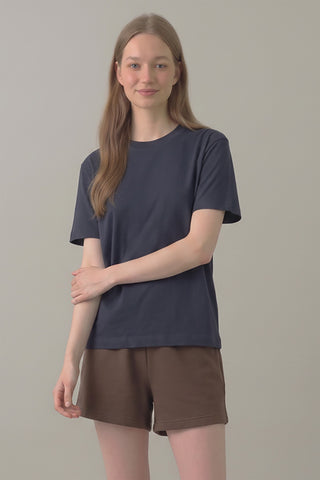 Woman wearing a navy blue t-shirt and brown shorts on a plain background