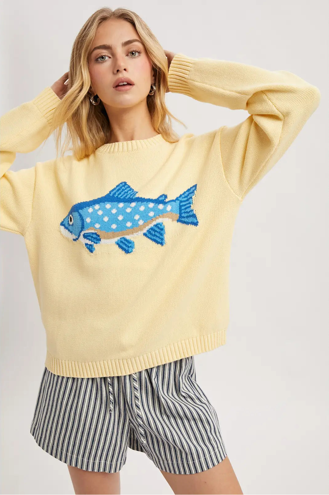 Woman wearing a yellow sweater with a blue fish design on a plain background