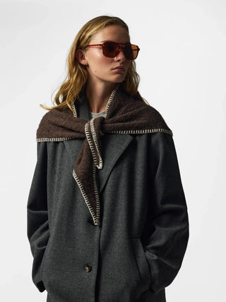 A woman wearing a dark gray wool coat with a brown suede-like collar trimmed with gold-toned stitching, styled with brown sunglasses against a light gray background.