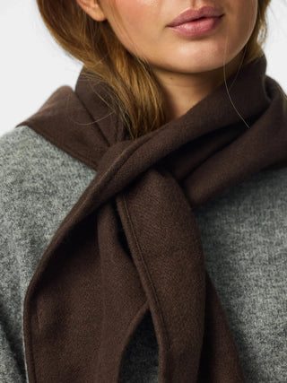 A close-up of a woman wearing a dark brown scarf tied around her neck over a gray knit sweater.