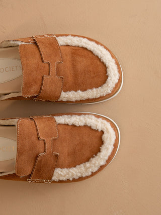 Pair of brown suede shoes with white fur lining on a beige background