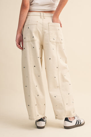 Beige pants with decorative studs worn by a person on a beige background