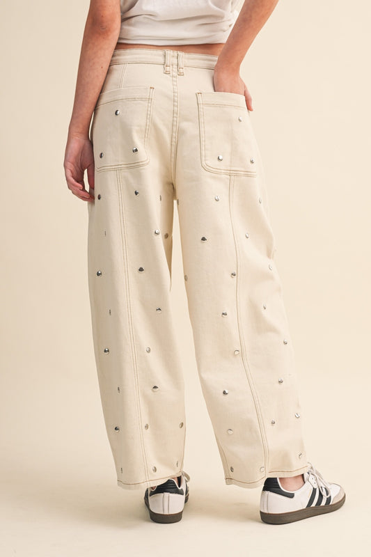 Beige pants with decorative studs worn by a person on a beige background