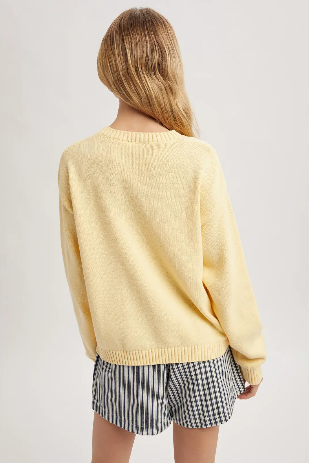 Person wearing a yellow sweater and striped shorts on a plain background