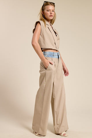 Woman wearing a beige sleeveless top and wide-leg pants against a plain background