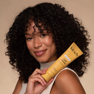 Woman holding a yellow tube of 'kitsch' hair product against a beige background