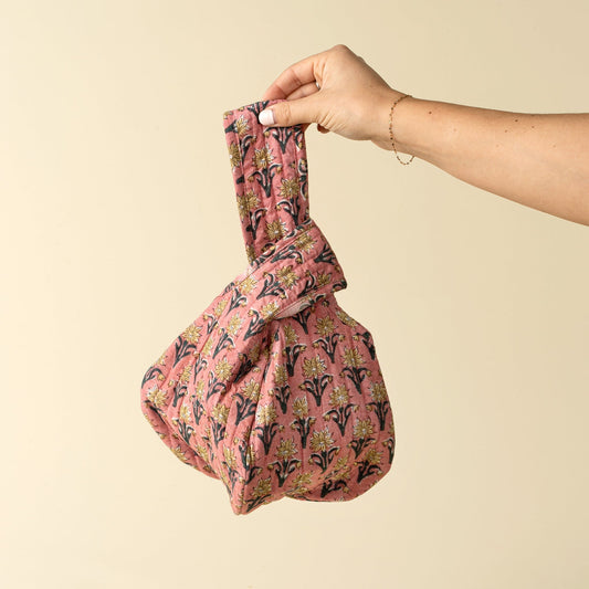 Hand holding a pink patterned bag against a beige background
