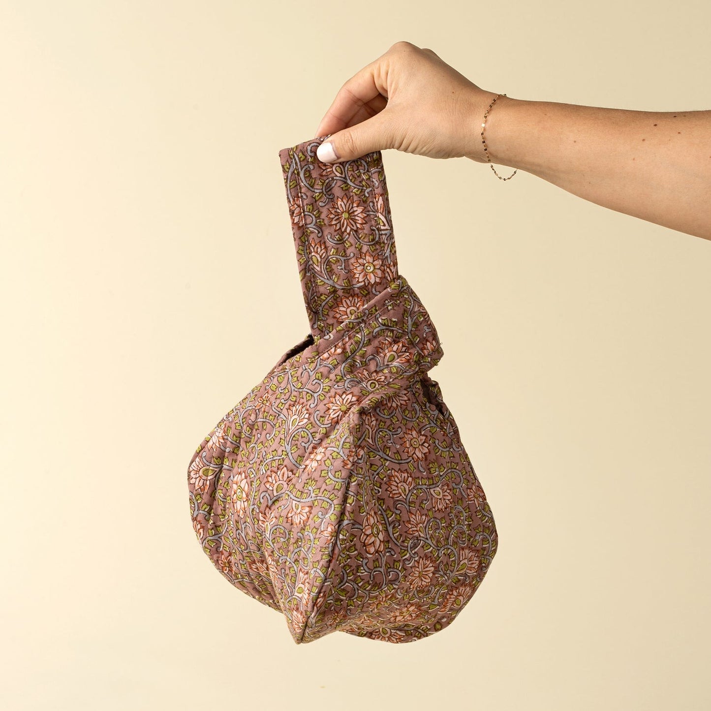 Hand holding a patterned fabric bag against a beige background