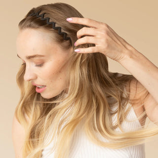 Woman combing her hair with a wide-tooth comb against a beige background