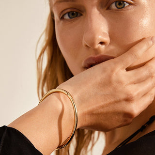Close-up of a woman's hand wearing a gold bracelet on a neutral background