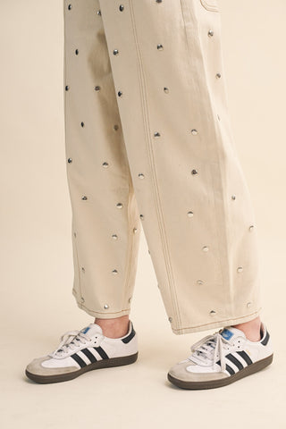 Person wearing beige pants with black embellishments and Adidas sneakers on a beige background