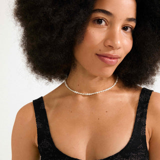 Woman wearing a black top and pearl necklace against a white background