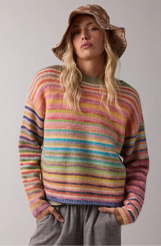 A women wearing a rainbow sweater against a neutral background.
