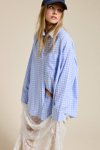 Woman wearing a blue checkered shirt over a lace dress with a cap on a beige background