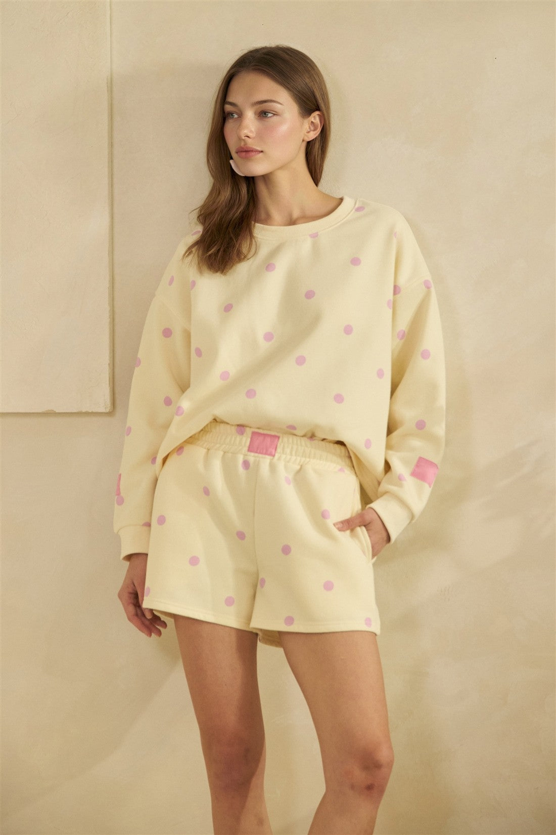Woman wearing a yellow outfit with pink polka dots against a beige background