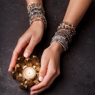 a women wearing multiple beaded wrap bracelets white holding a candle