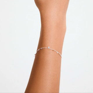 A delicate silver chain bracelet with small clear stones and a central round stone, shown worn on a person's wrist against a plain white background.