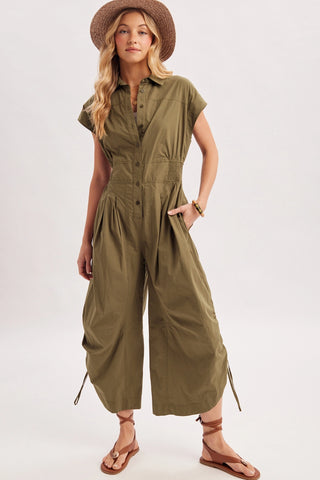 Woman wearing an olive green jumpsuit and straw hat on a white background