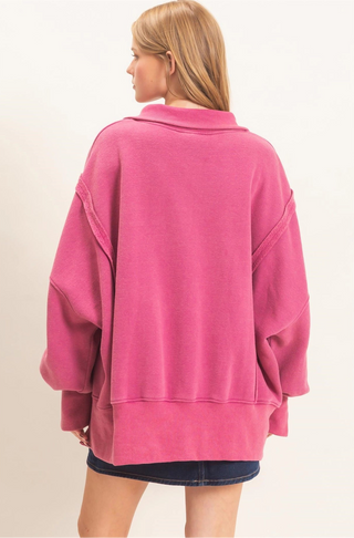 A woman shown from the back wearing an oversized pink sweatshirt and a dark denim skirt against a plain light beige studio background.