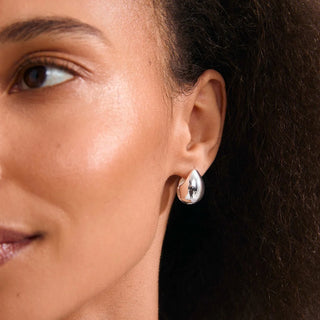 A close-up of a woman's ear wearing a polished silver teardrop-shaped stud earring with a small black accent at the center.