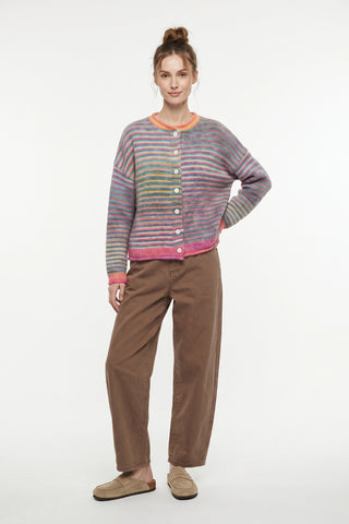 A woman modeling a multicolor striped knit cardigan with a button-up front, paired with brown pants and beige slip-on shoes, against a plain white studio background.